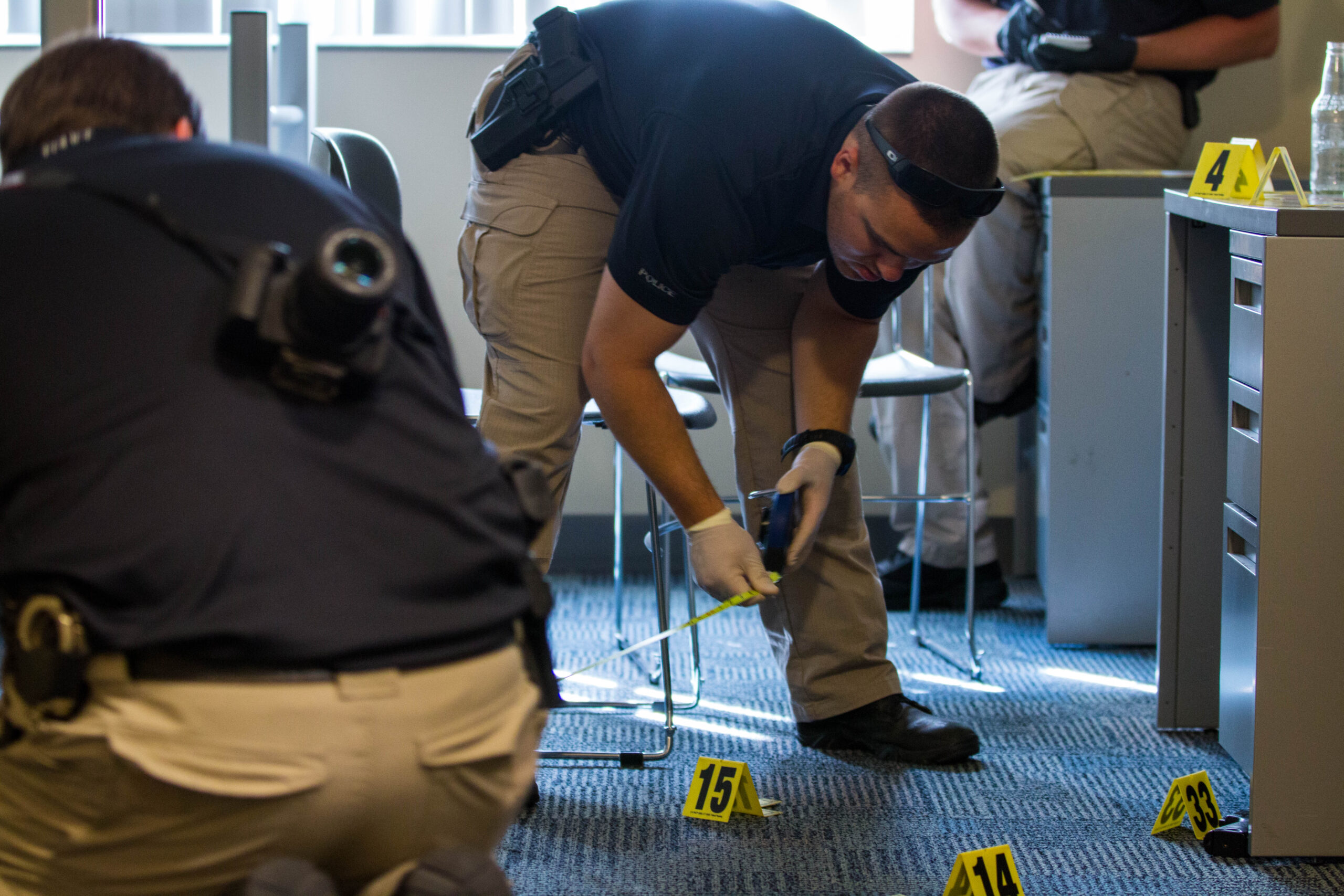 Students in the crime scene specialist class are shown placing numbered evidence markers by pieces of evidence